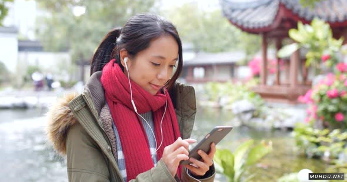 湖边的女人听耳机，用手机上网实拍4K视频Woman listen to earphone and surf the internet on mobile phone in china