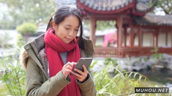 女人穿着冬装和使用手机在中国花园4K视频Woman wearing winter jacket and use of mobile phone in china garden插图