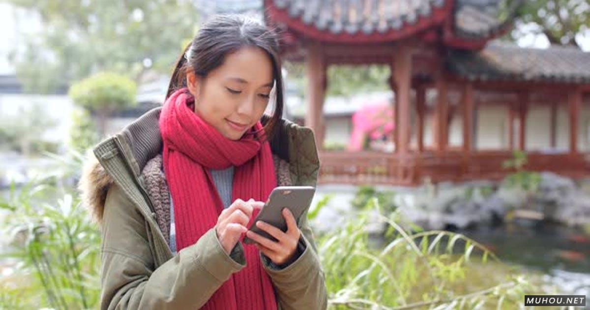 女人穿着冬装和使用手机在中国花园4K视频Woman wearing winter jacket and use of mobile phone in china garden