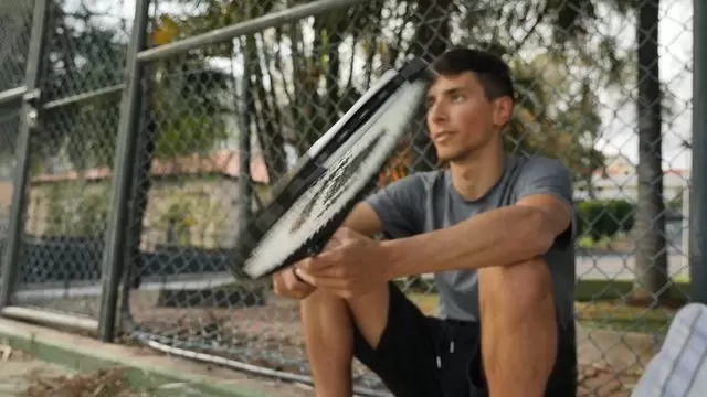 男子坐在地上旋转网球拍视频素材