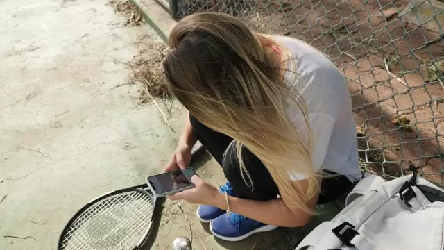 一名妇女坐在网球场上使用手机视频素材