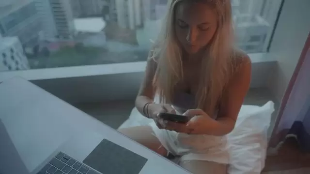 一个女孩坐在她的桌子旁，在她的手机和笔记本电脑上工作视频素材